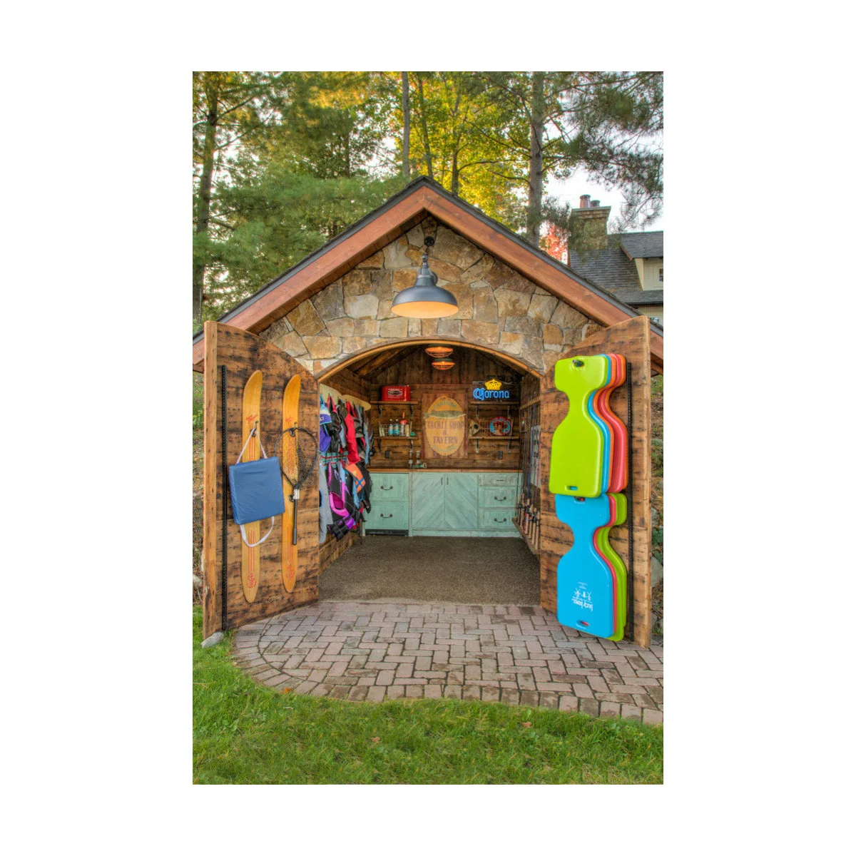 Small stone-fronted garden building with open timber doors holding recreation equipment and pale green bar cabinets inside