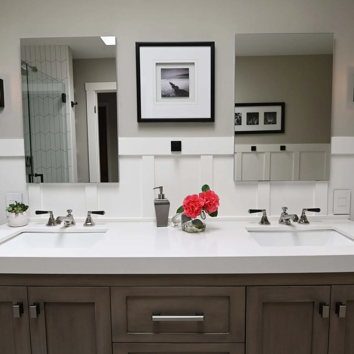 Two plain rectangular mirrors above a white double-basin counter and gray vanity with a small framed picture between them.