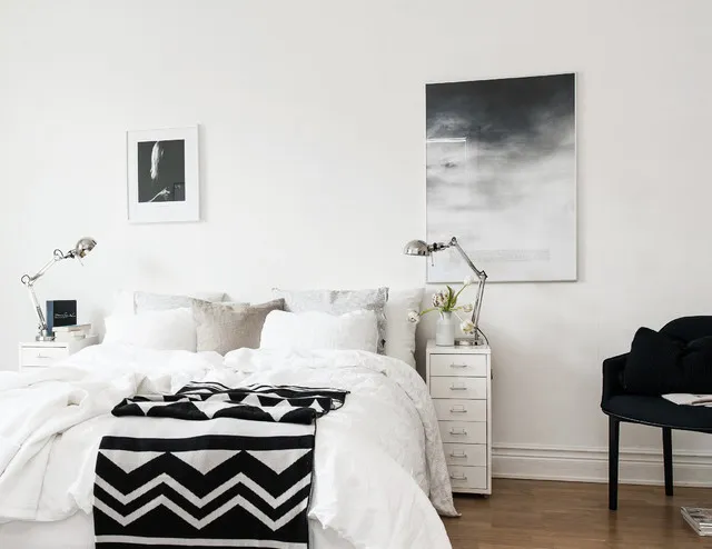 A pale bed sits beneath a few framed prints beside a dark chair.
