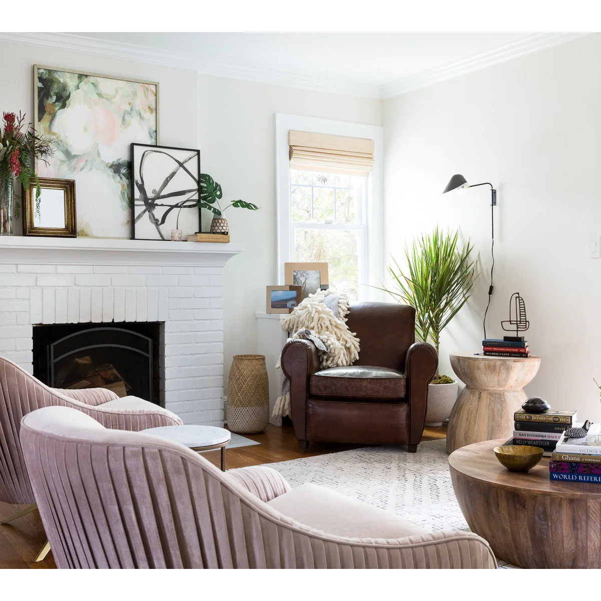 White fireplace corner with a dark brown armchair, pink chairs and wood tables