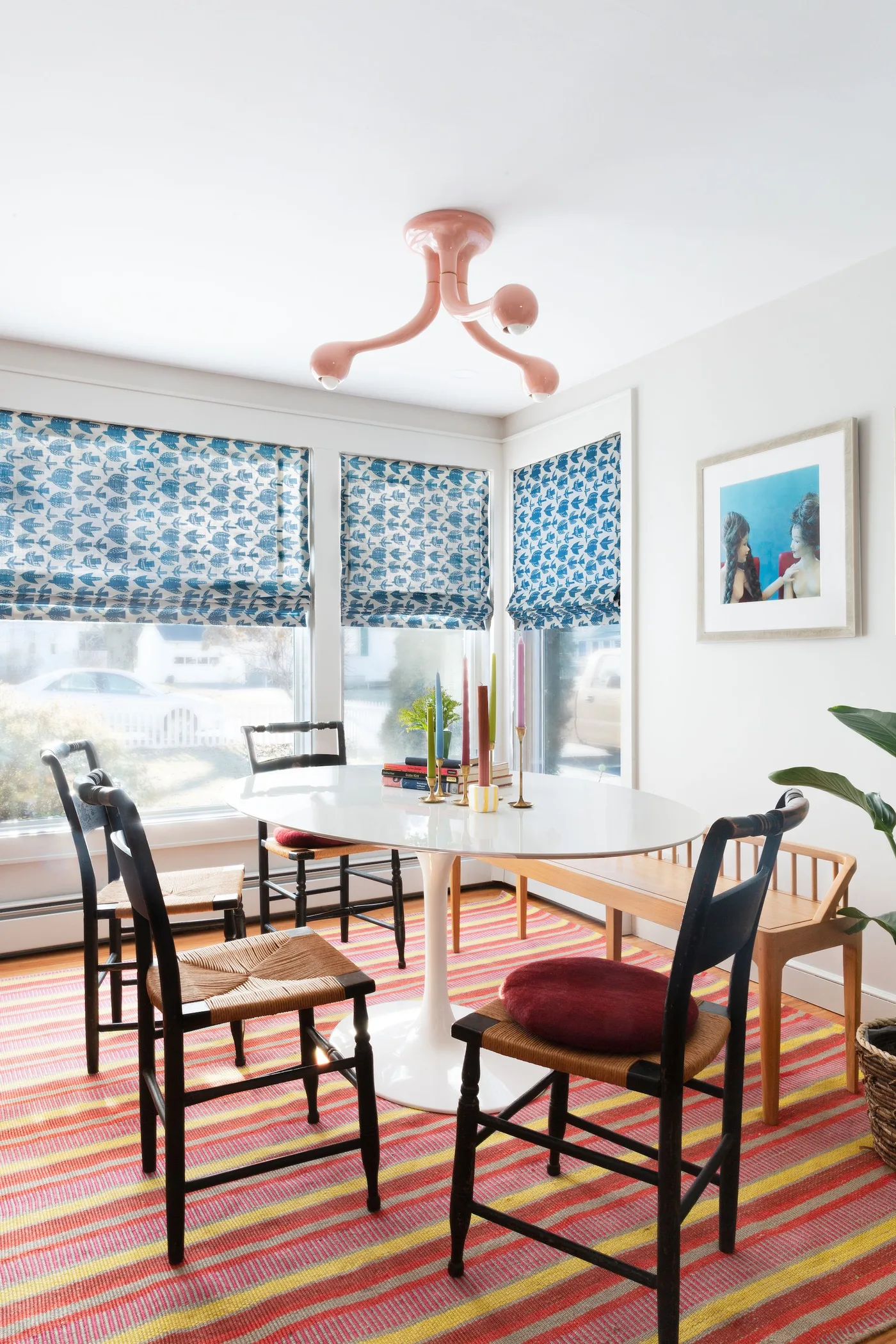 White roundeded dining table with black wooden chairs, blue patterned blinds and a pink striped rug.
