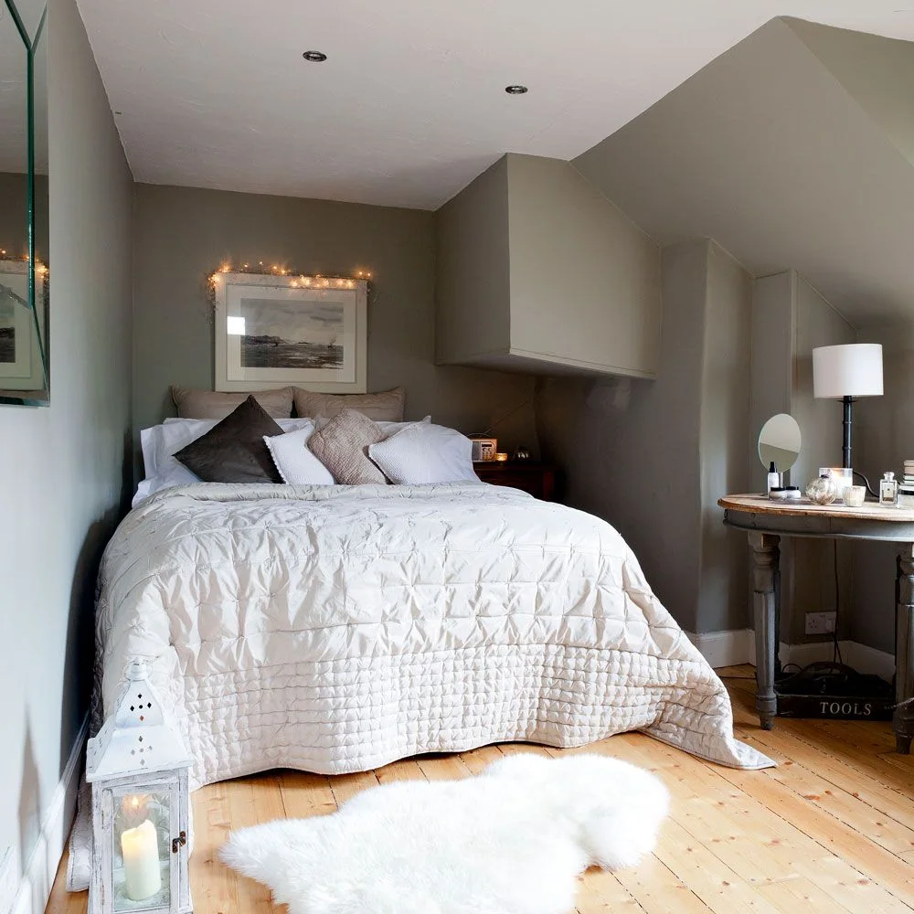 White-covered bed in a gray attic alcove beside a projecting wall and a separate small dressing table.