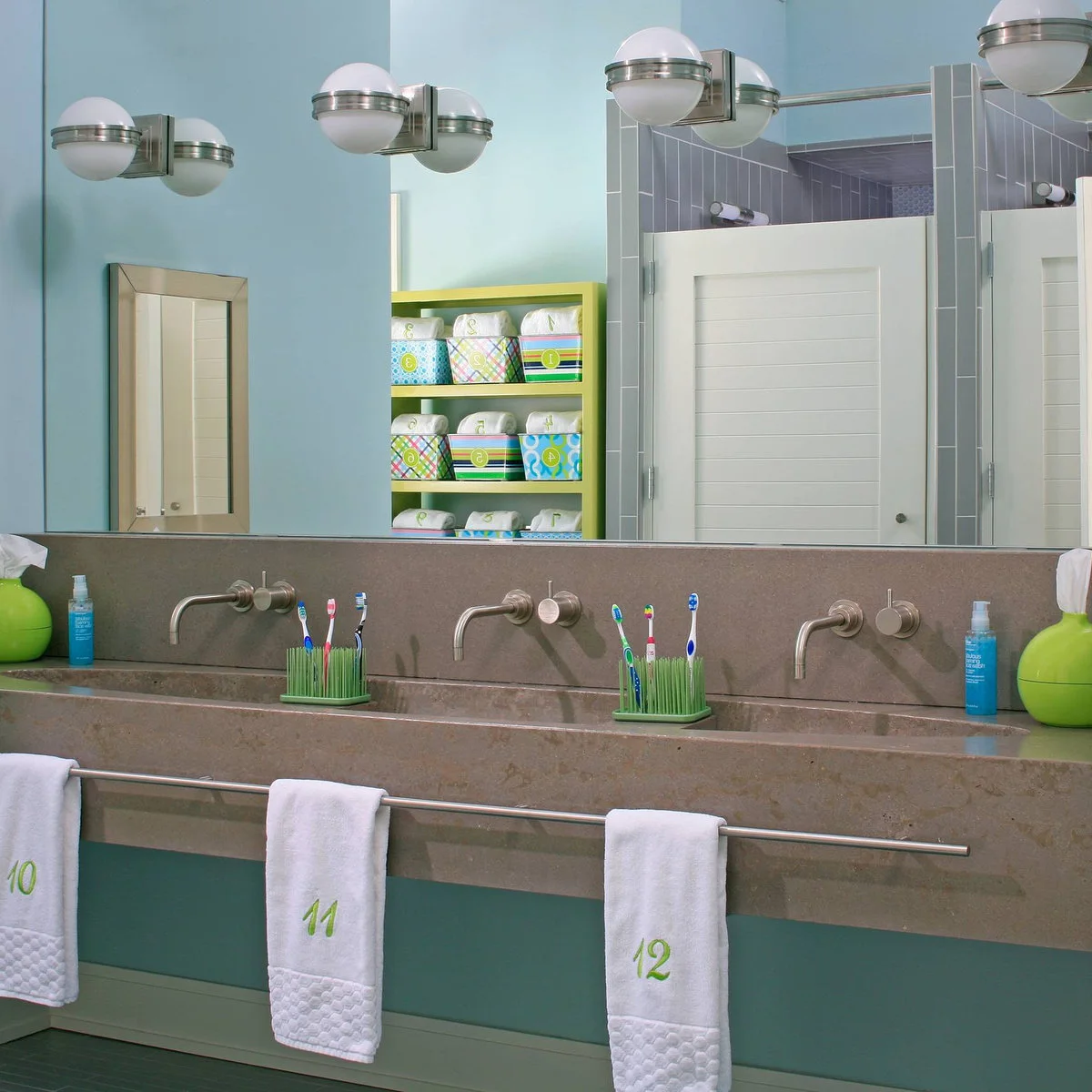 Three numbered white hand towels hang from a long front rail below a trough sink with three wall-mounted faucets.