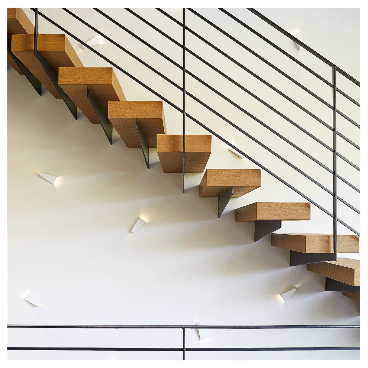 Open wood staircase with black horizontal railing and small angular wall lights below the treads