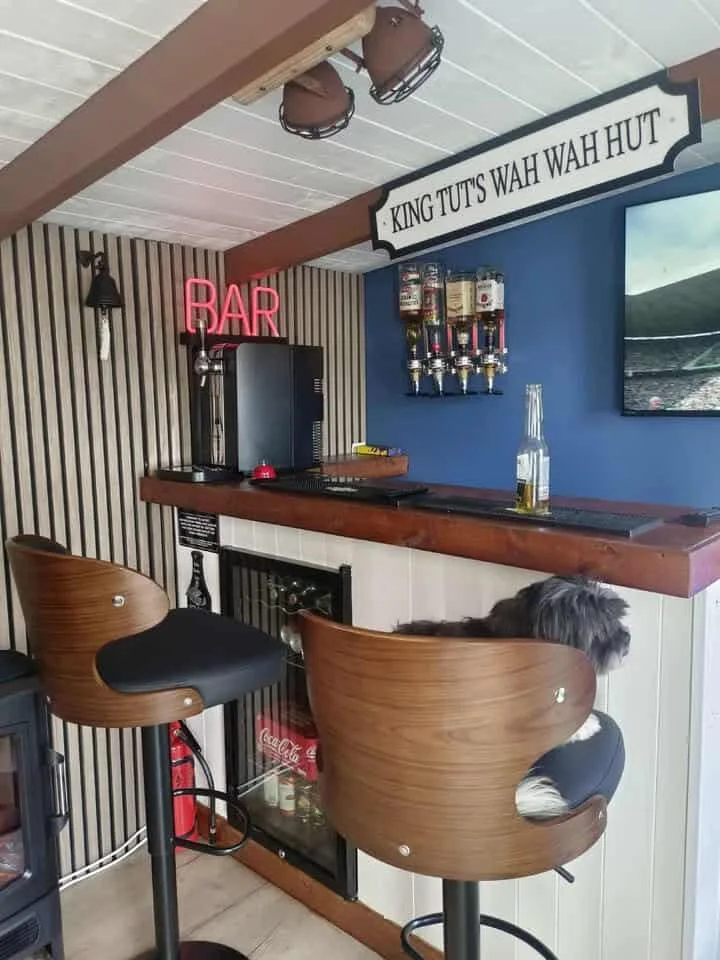 Compact shed bar with a wood counter, dark blue wall, slatted side wall and two stools