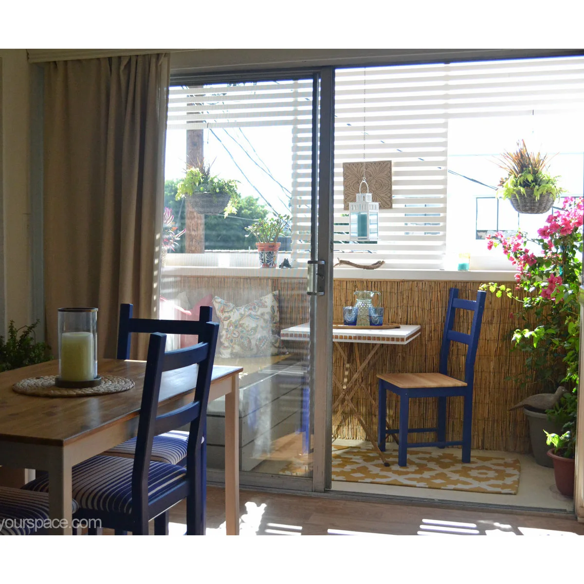 View through sliding doors to a small planted balcony with blue chair and bench