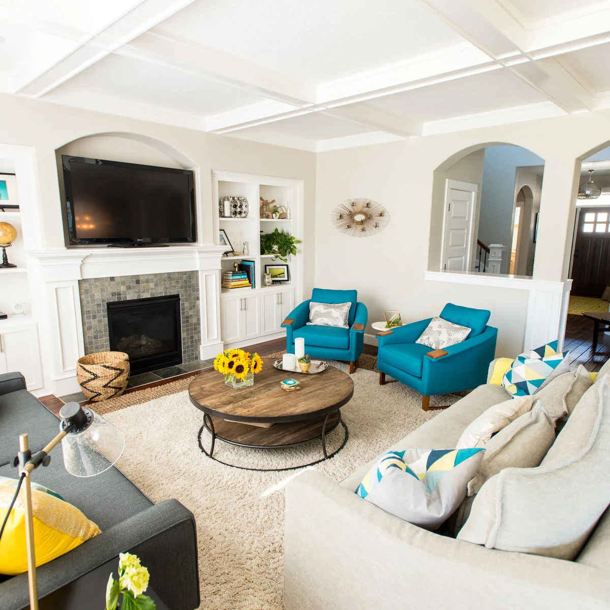 Round wooden coffee table with yellow flowers, a tray and coasters beside teal chairs