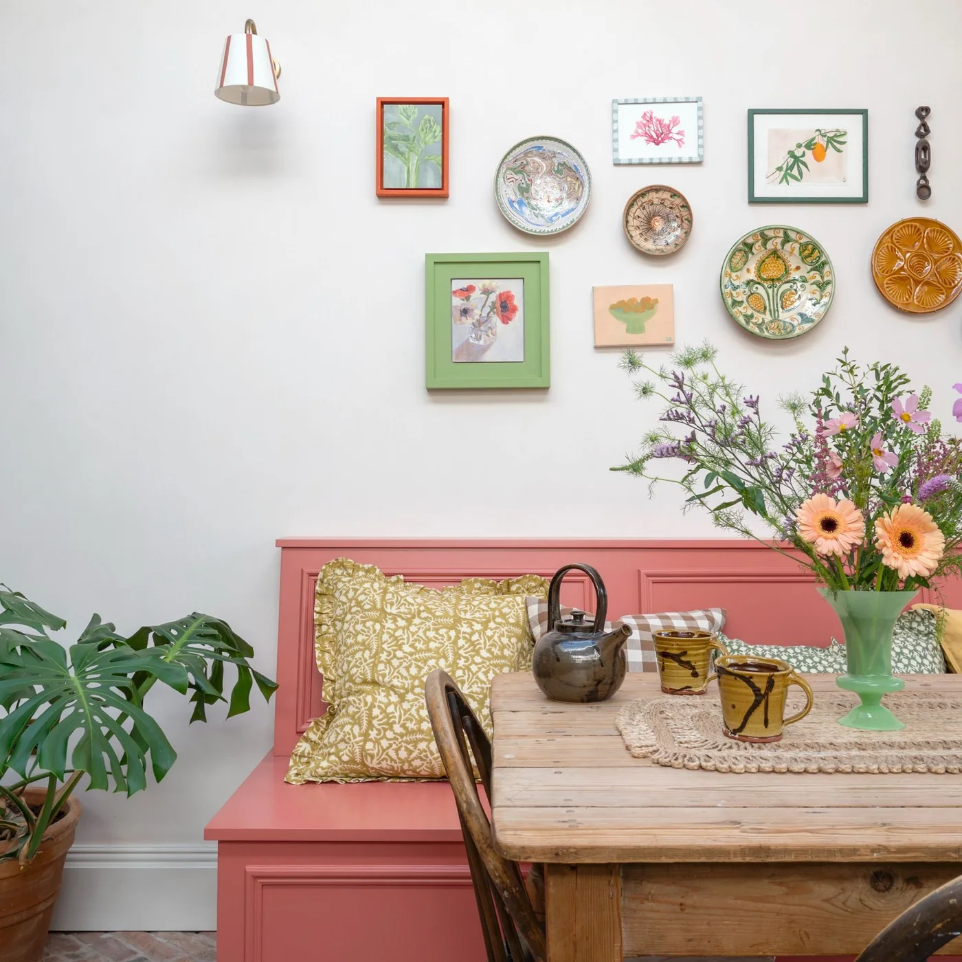 Colorful framed botanical pictures and decorative plates above a pink dining bench