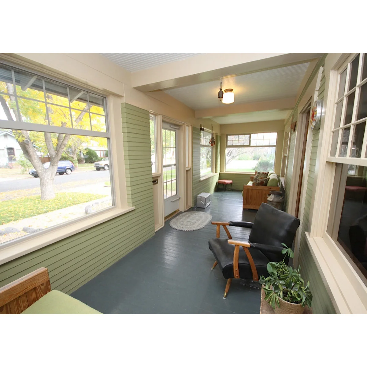 A long enclosed porch with green siding, a dark armchair near the door and a bench at the far end.