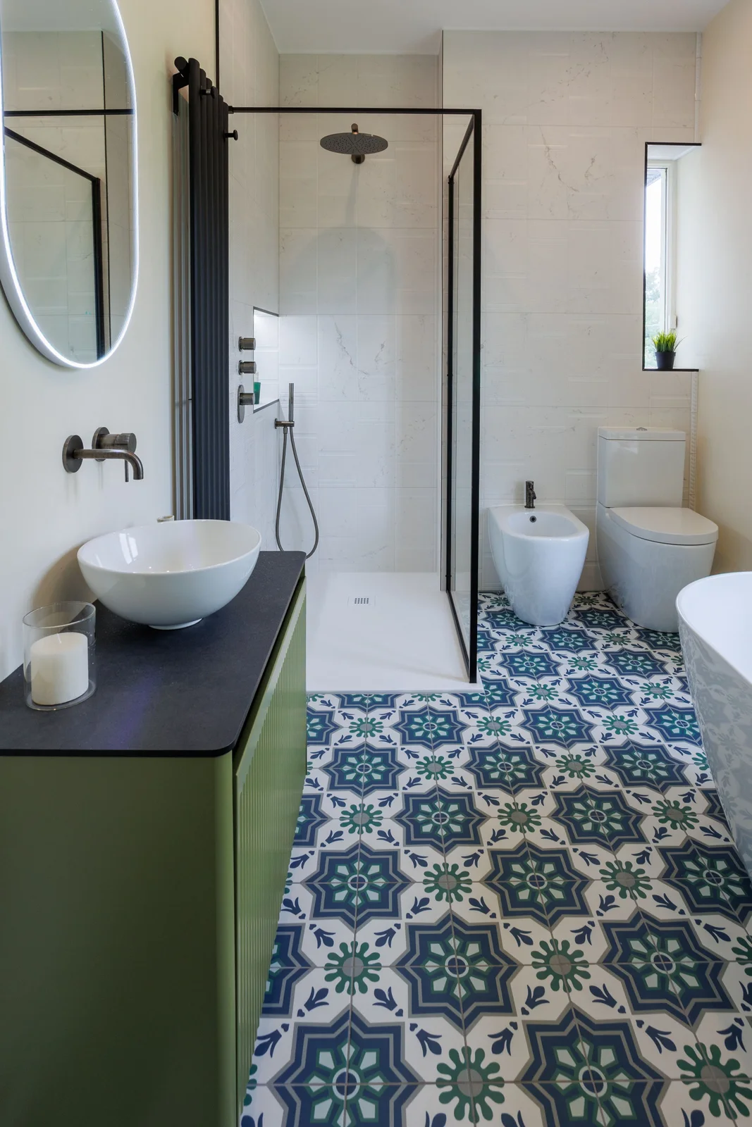 A reeded olive floating vanity with a dark top and white vessel basin sits above a blue, green and white patterned bathroom floor.