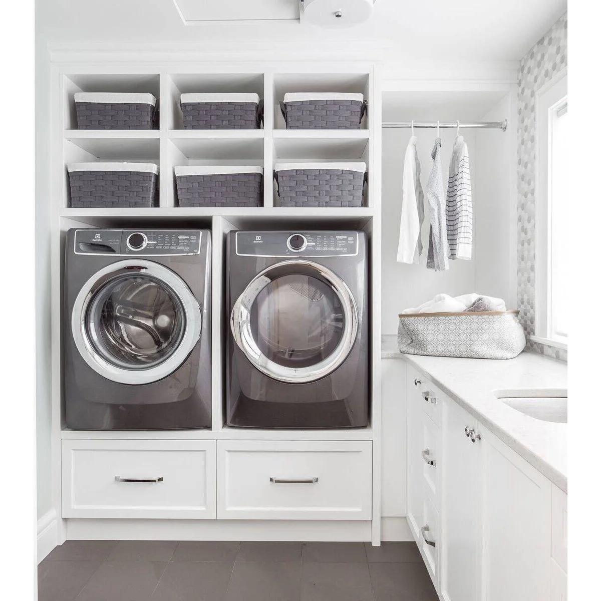 Laundry room with two gray appliances above white drawers, six basket cubbies overhead and a sink counter to the right