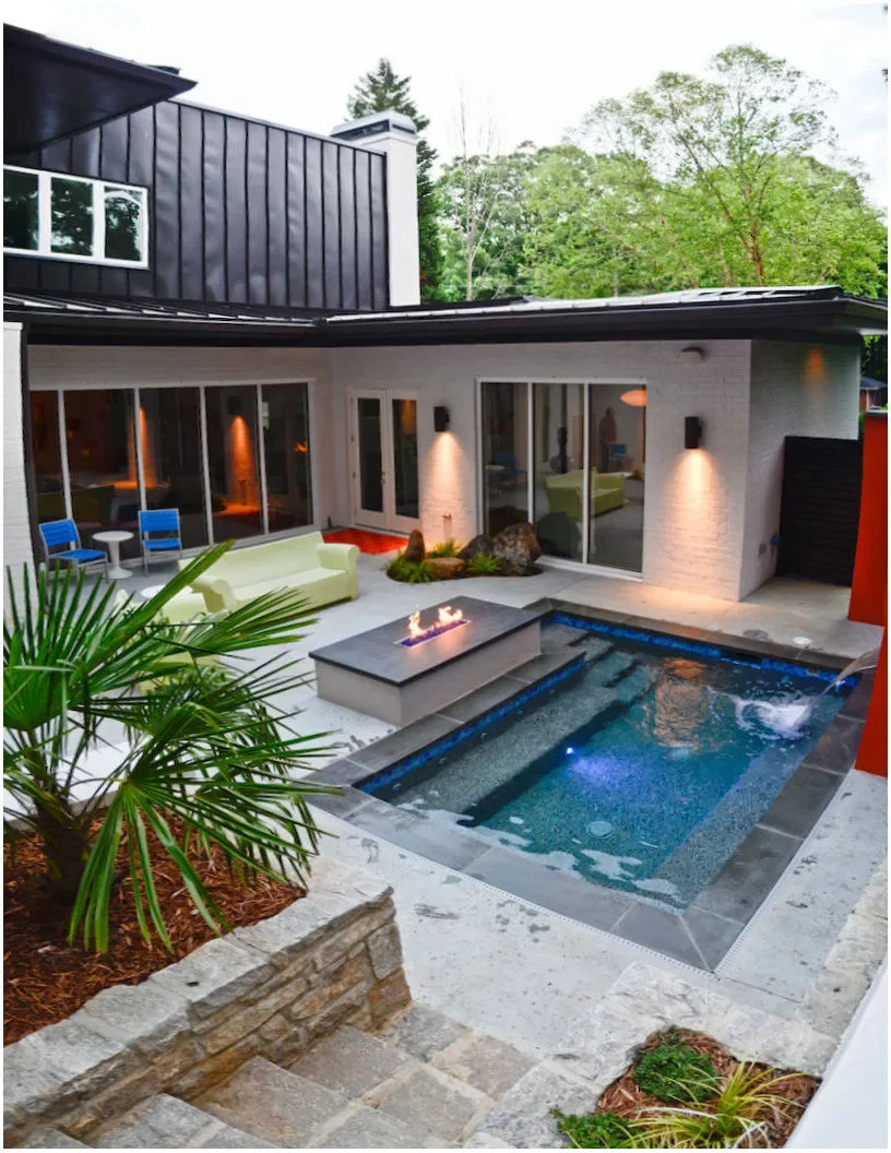 A small rectangular courtyard pool has a long submerged bench, a wall spout and an adjoining patio with seating.