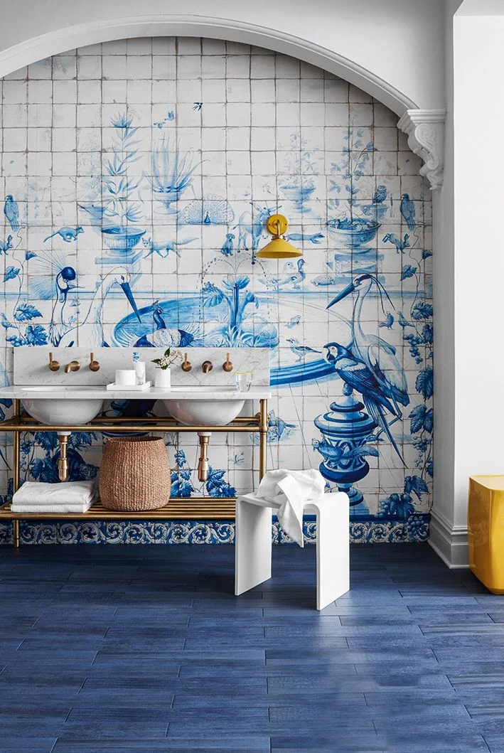 A double basin stands beneath a large blue-and-white scenic mural within an arched wall beside yellow accents and a blue floor