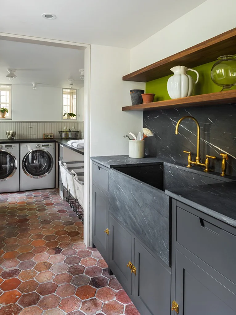 Mixed rust and brown hexagonal tiles run from a dark sink counter into a laundry room.