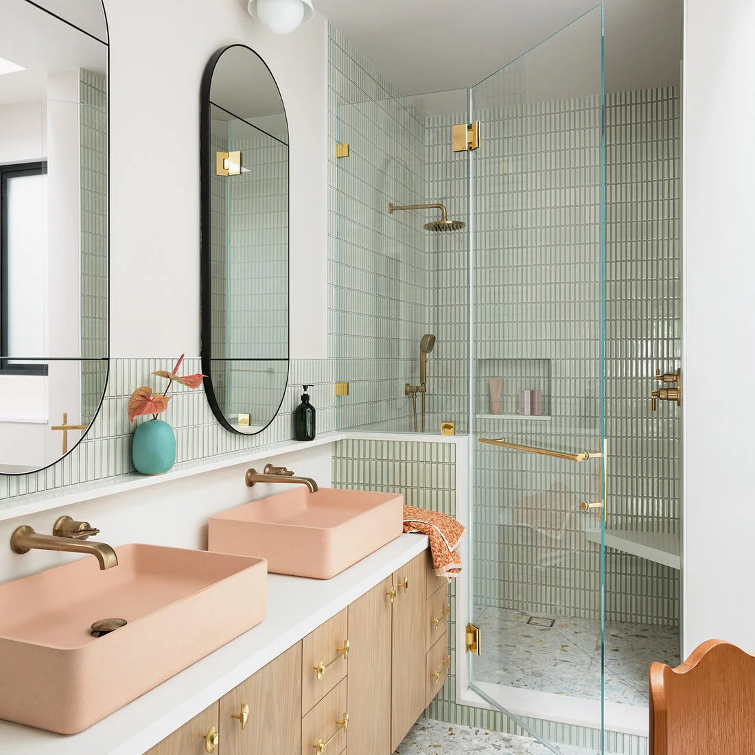 Peach rectangular basins face a glass shower with narrow green tiles and a pale terrazzo floor.