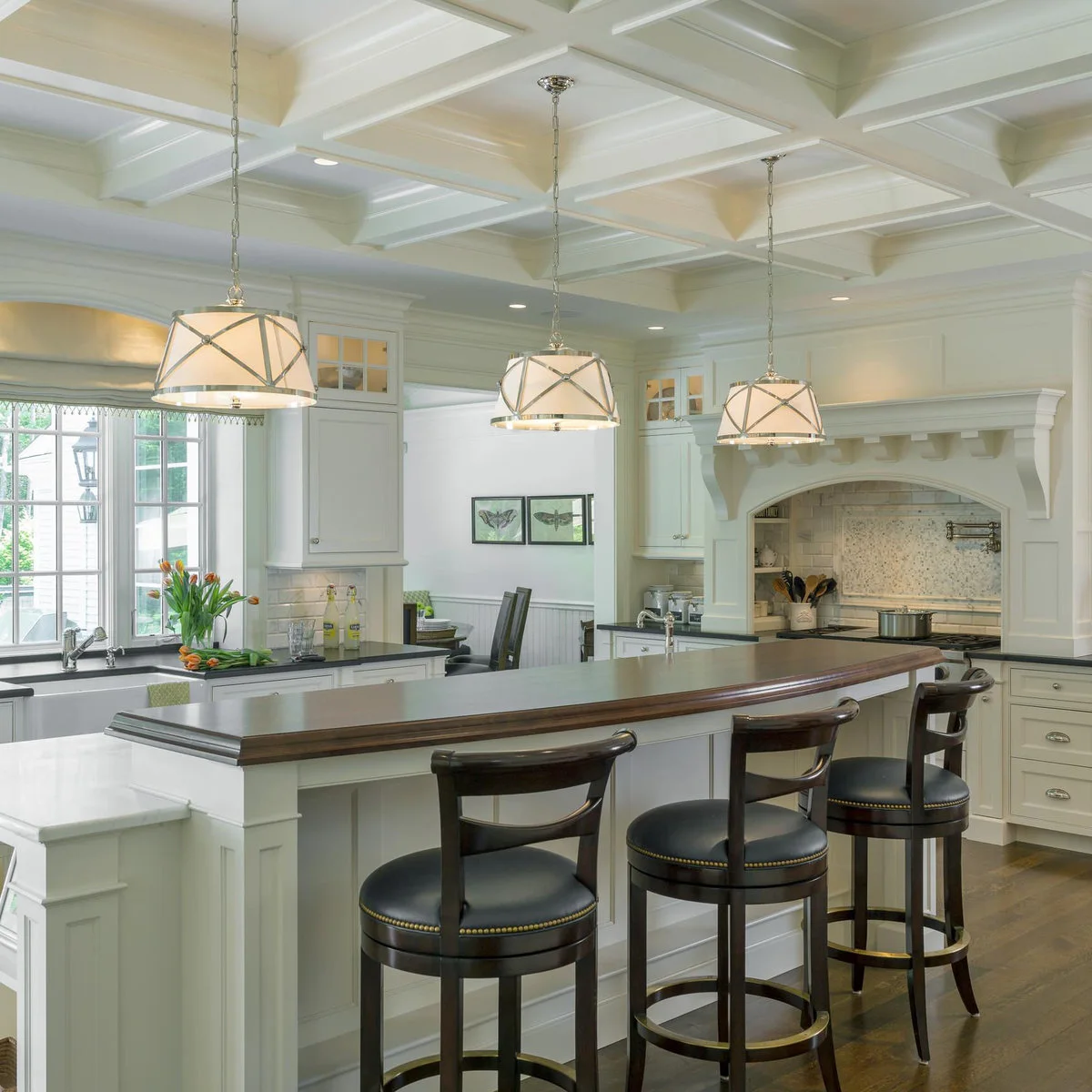 Dark wood kitchen stools with rounded backs, padded seats and metal-colored circular foot rails at a raised counter