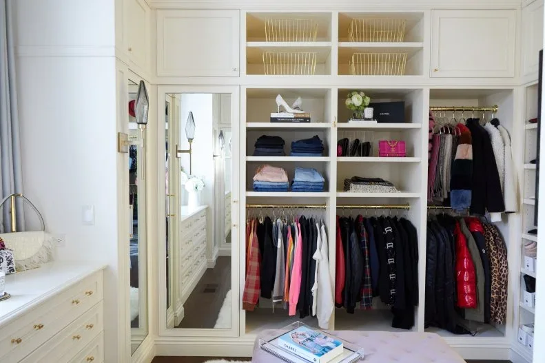 White closet shelves combine folded clothing, two levels of short hanging, upper baskets and a tall mirrored door.
