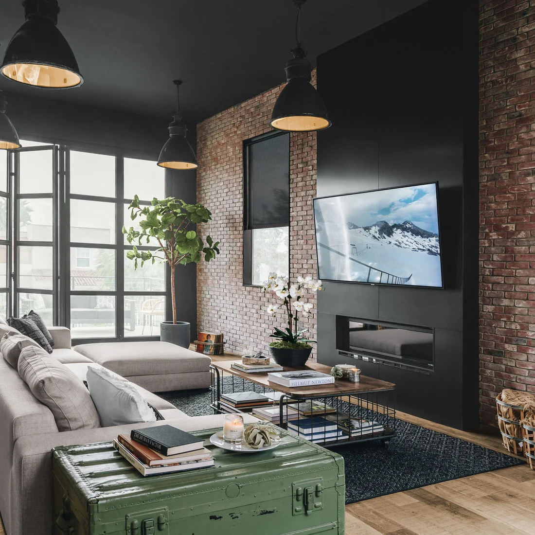 A pale sectional and green metal trunk beneath black pendants beside a brick fireplace wall