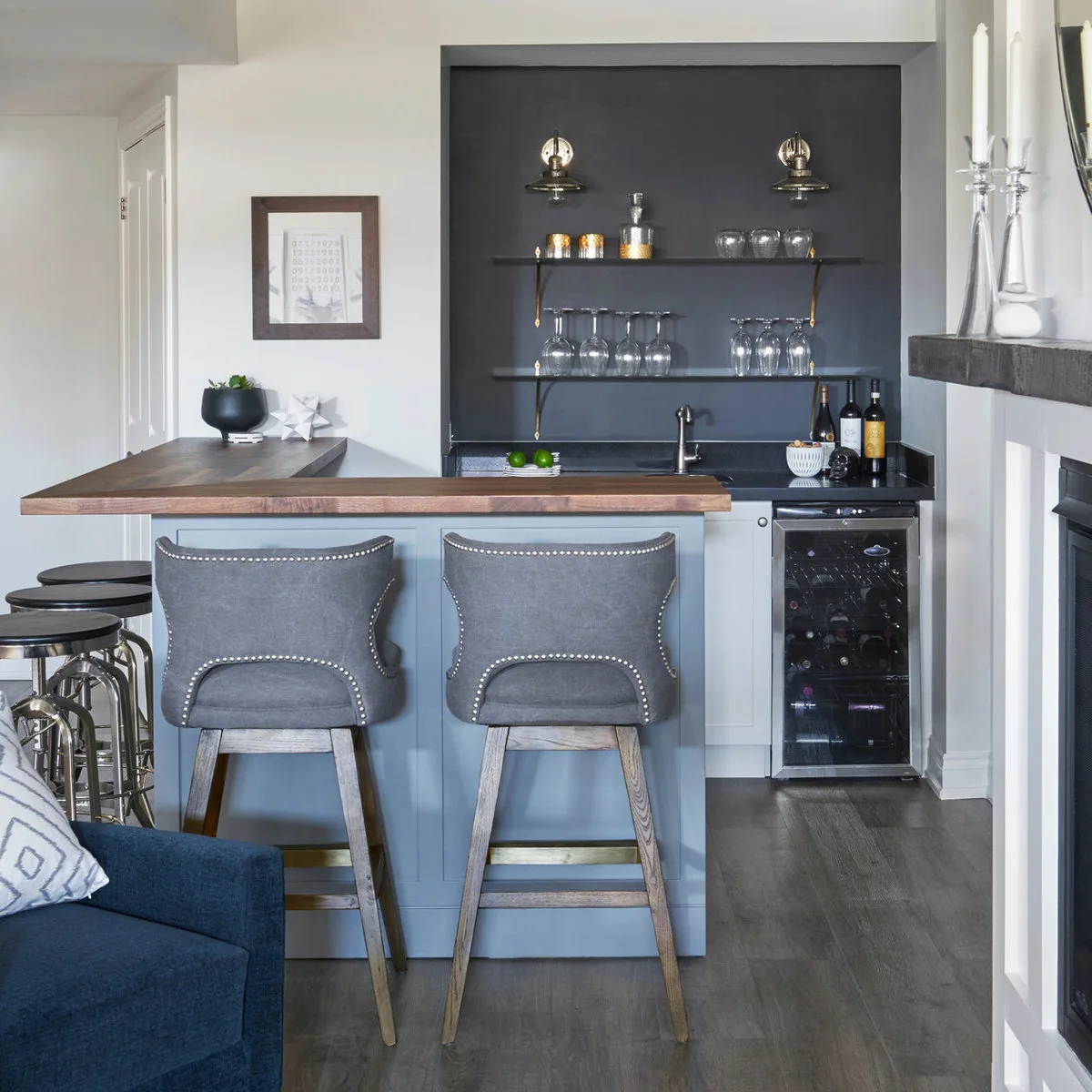 Compact gray home bar with short wood seating return, upholstered stools, rear sink and open shelves
