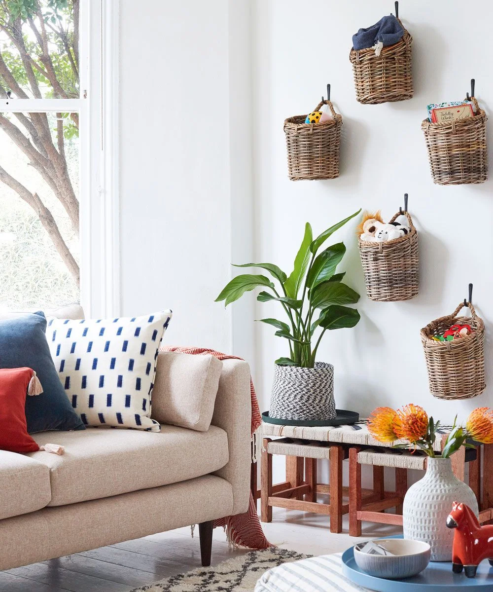 Woven wall baskets holding books, toys and soft animals beside a pale living-room sofa