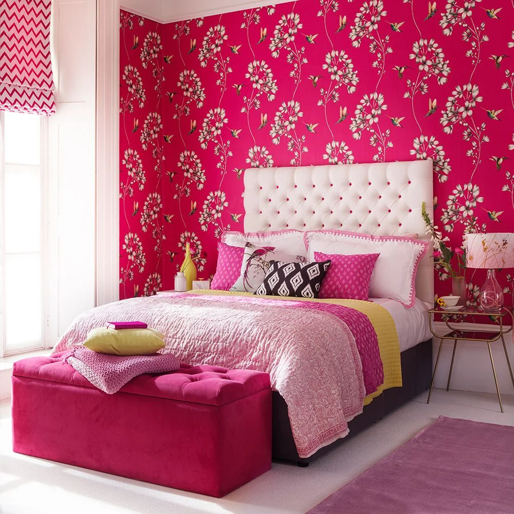 White blossoms and small birds repeat on hot pink wallpaper behind a pale tufted headboard.