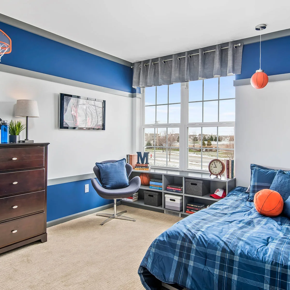 Blue and white boy’s bedroom with window-side cubbies, a reading chair and basketball accents