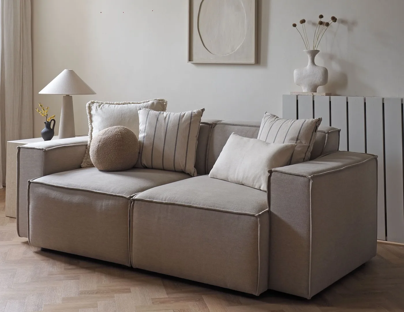 The same pale sofa with a round textured pillow, striped squares and plain rectangular pillows.