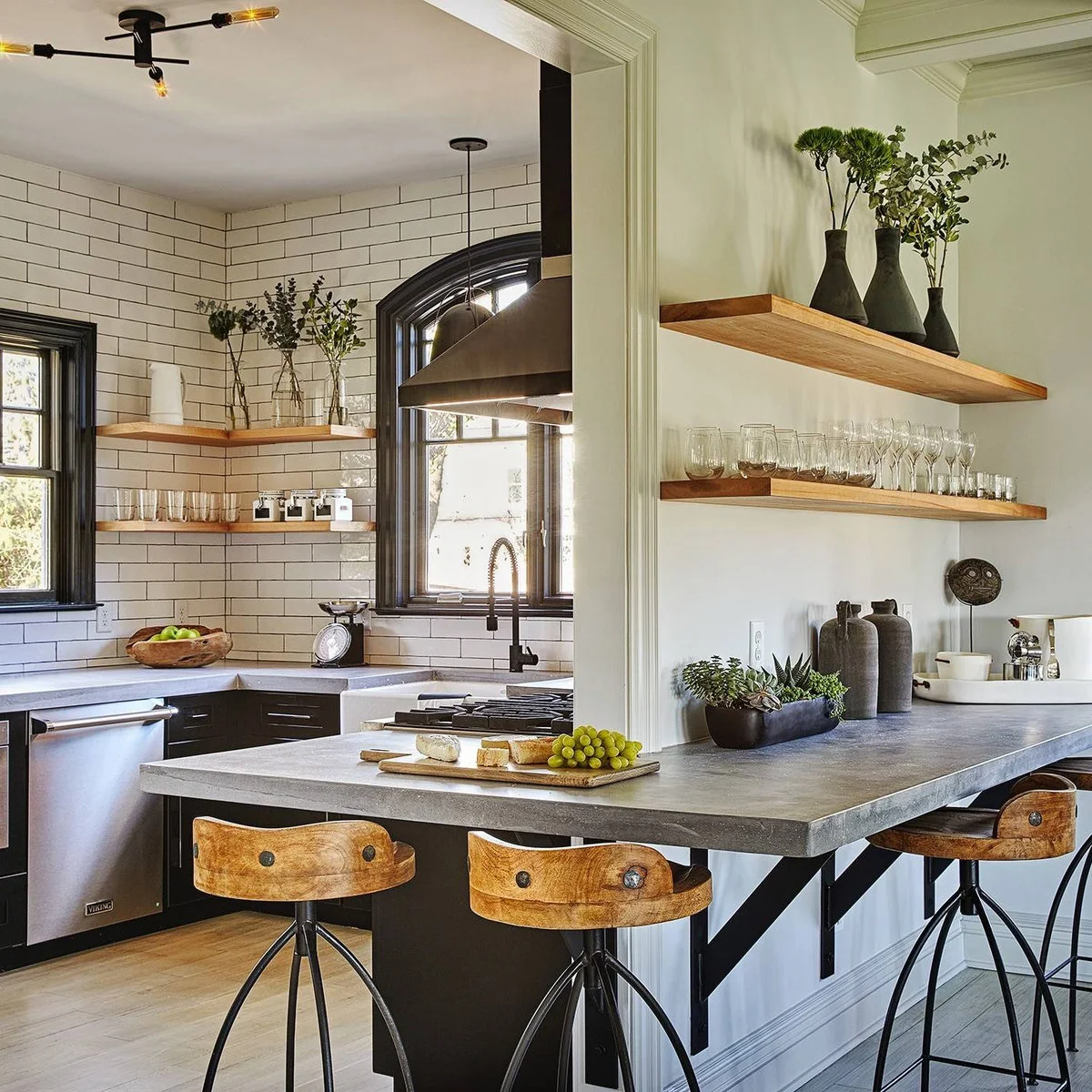 A partial wall with wood shelves sits above a pale breakfast counter beside a black-and-white kitchen.