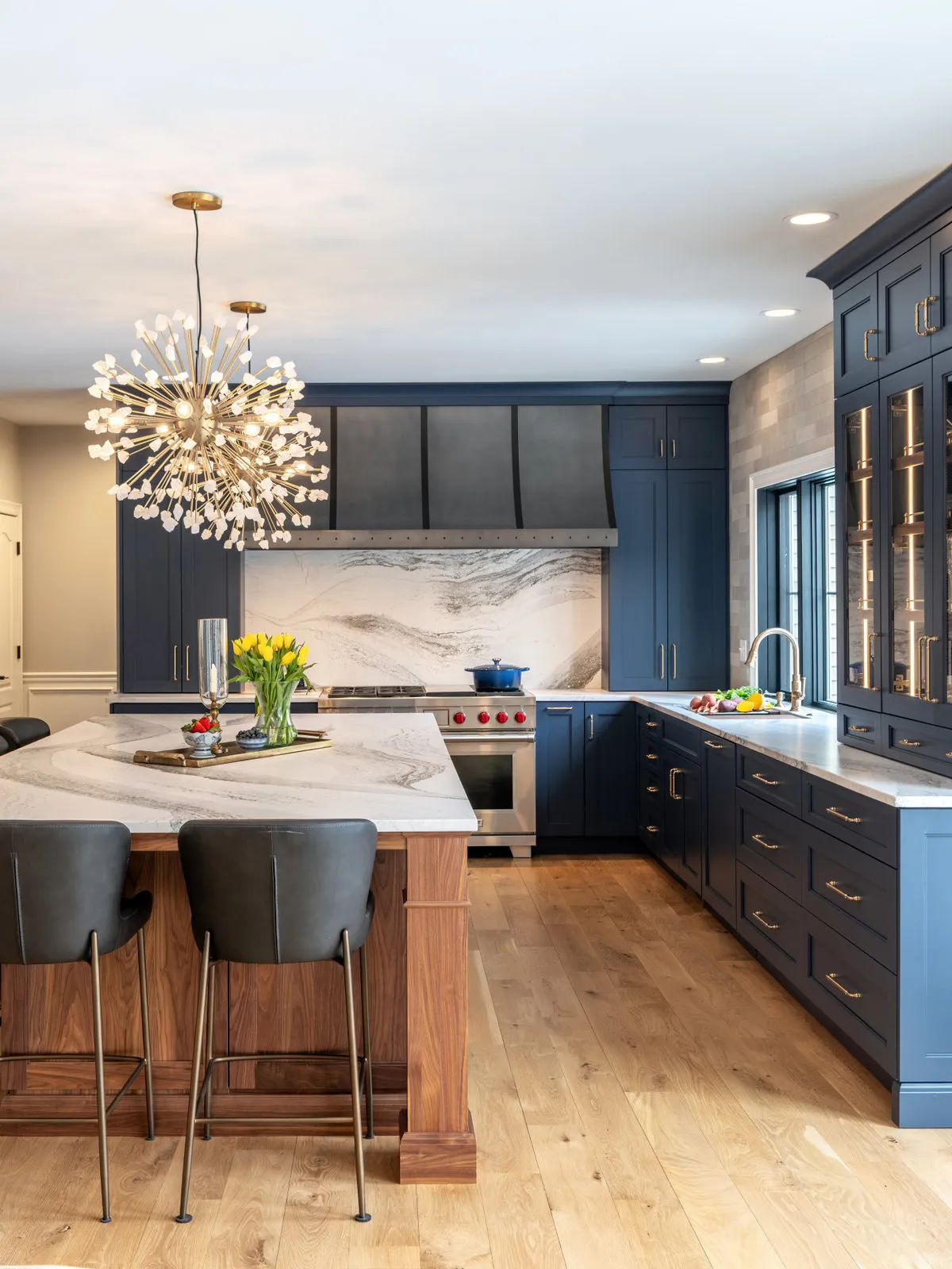 Deep blue cabinets surround a timber island with a pale veined counter beneath a decorative pendant.