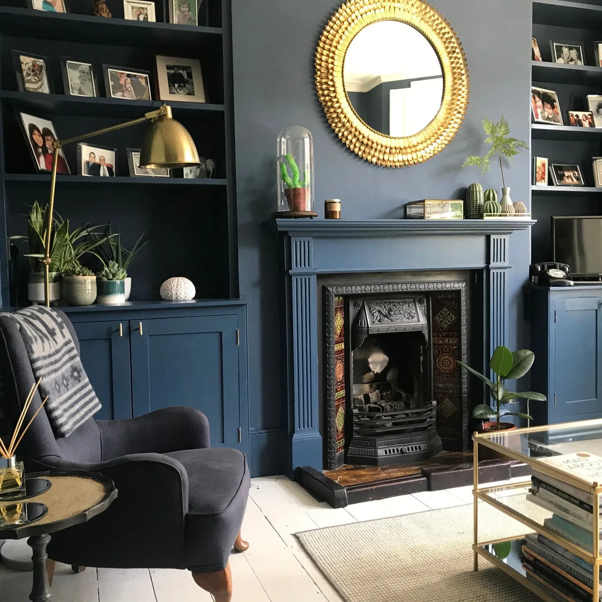 Dark blue terrace sitting room with matching alcove cupboards, tiled fireplace and round gold-colored mirror