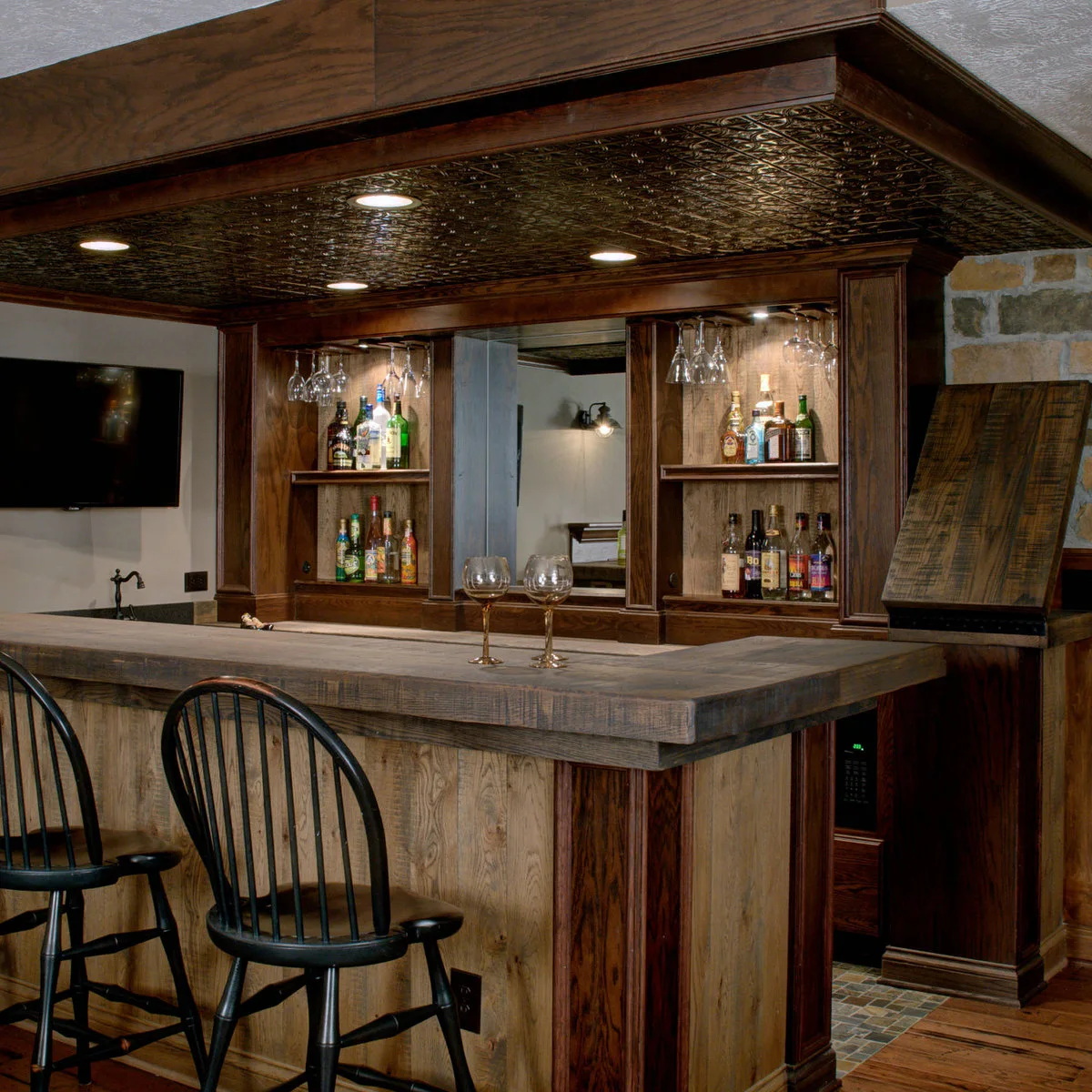 Traditional wood-colored basement bar with black stools, mirror and glass storage