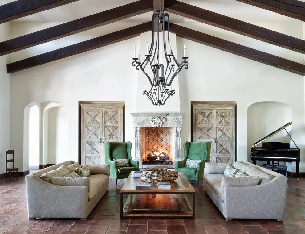 Green accent chairs sit between pale sofas beneath dark timber ceiling beams