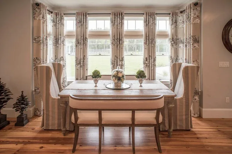 Wooden dining table with striped high-backed end chairs, a bench and pale patterned curtains.