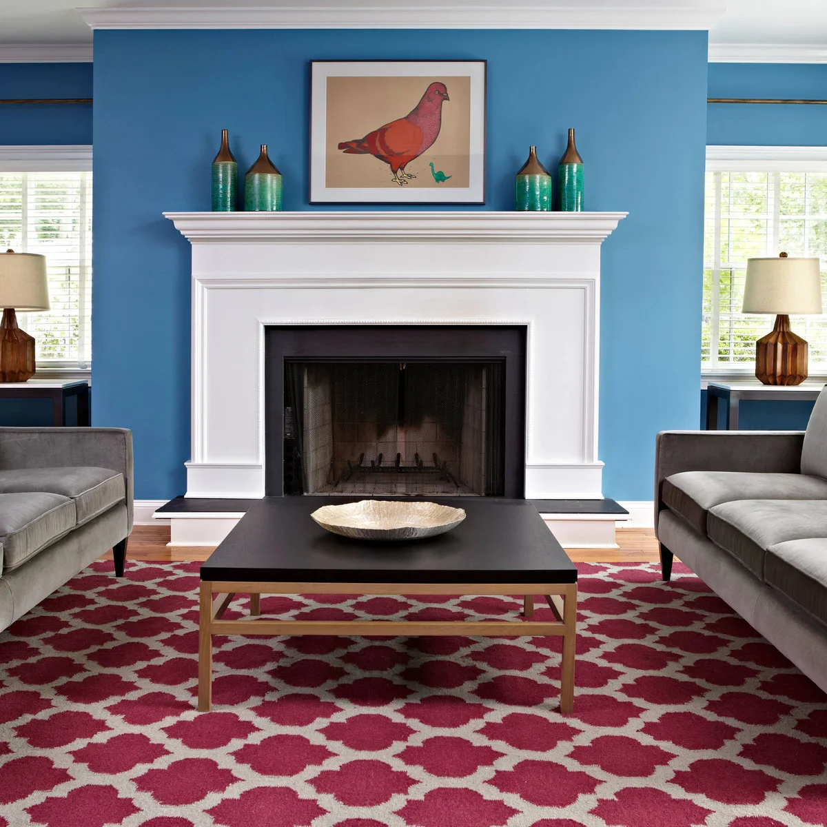 Gray sofas face each other across a dark table with blue walls and a raspberry patterned rug.