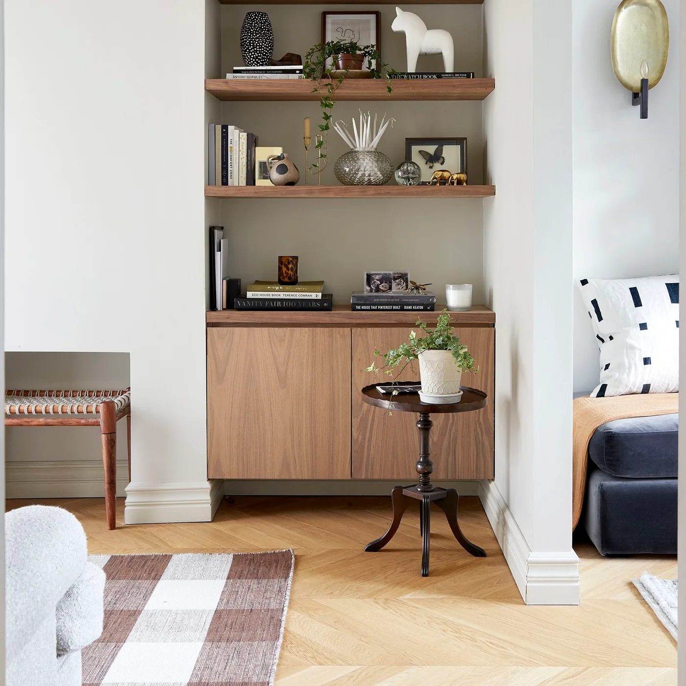 Wood shelves and lower cupboard in a pale living room beside a small dark side table and checked rug