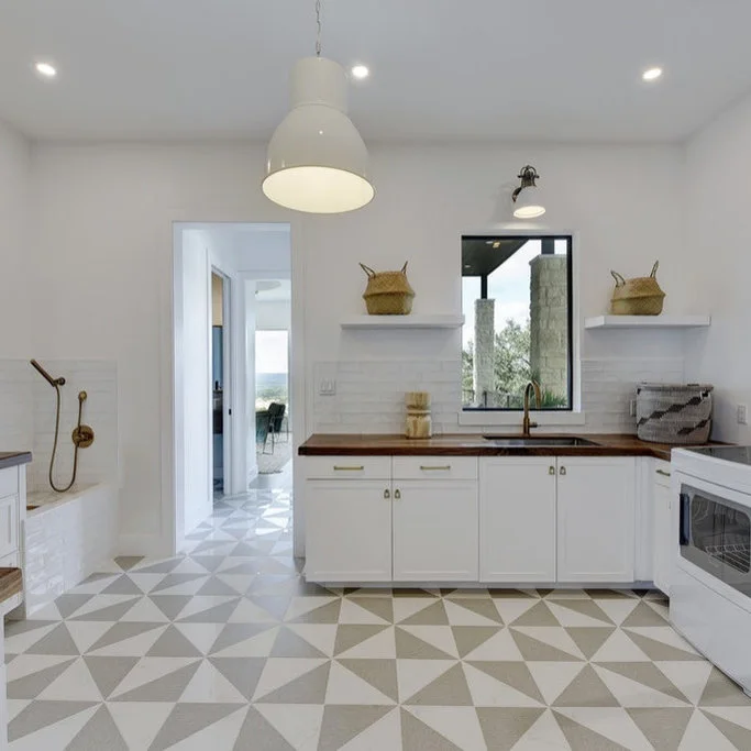 White utility cabinets and a wood counter face a geometric pale floor beside a low wash area with a wall-mounted sprayer.