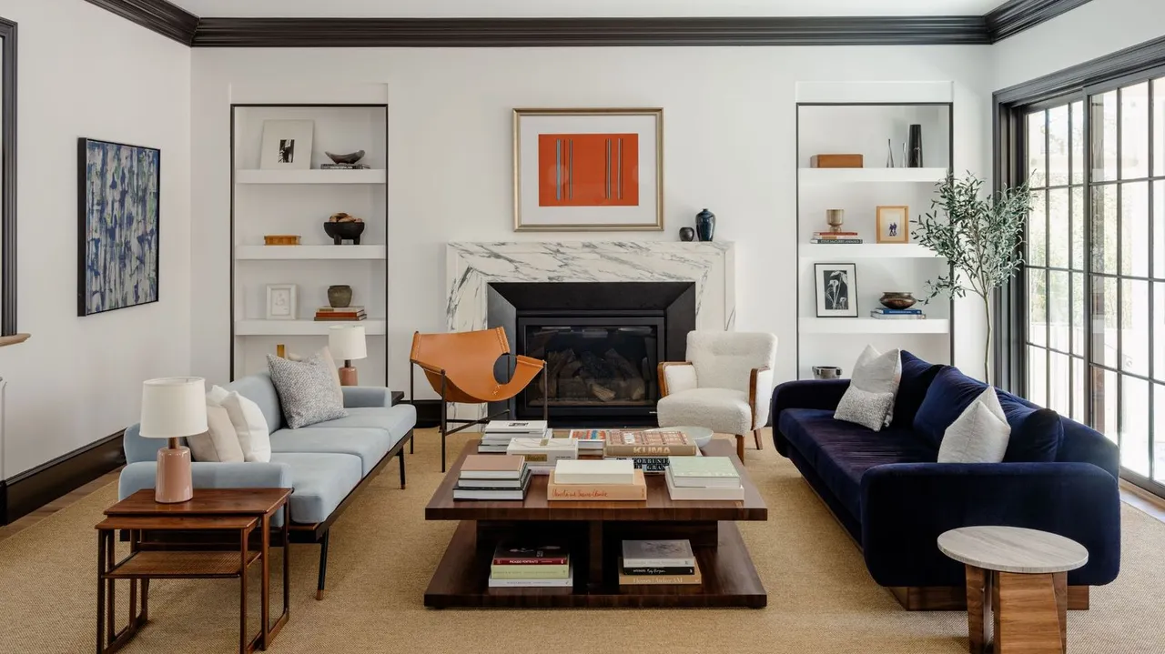 A navy sofa faces a pale blue sofa across a timber table, with light chairs beside a black fireplace and tall windows.