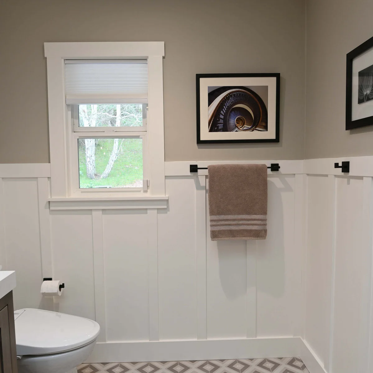 White board-and-batten lower wall with dark towel rail and hooks beneath a taupe painted wall and framed photograph.