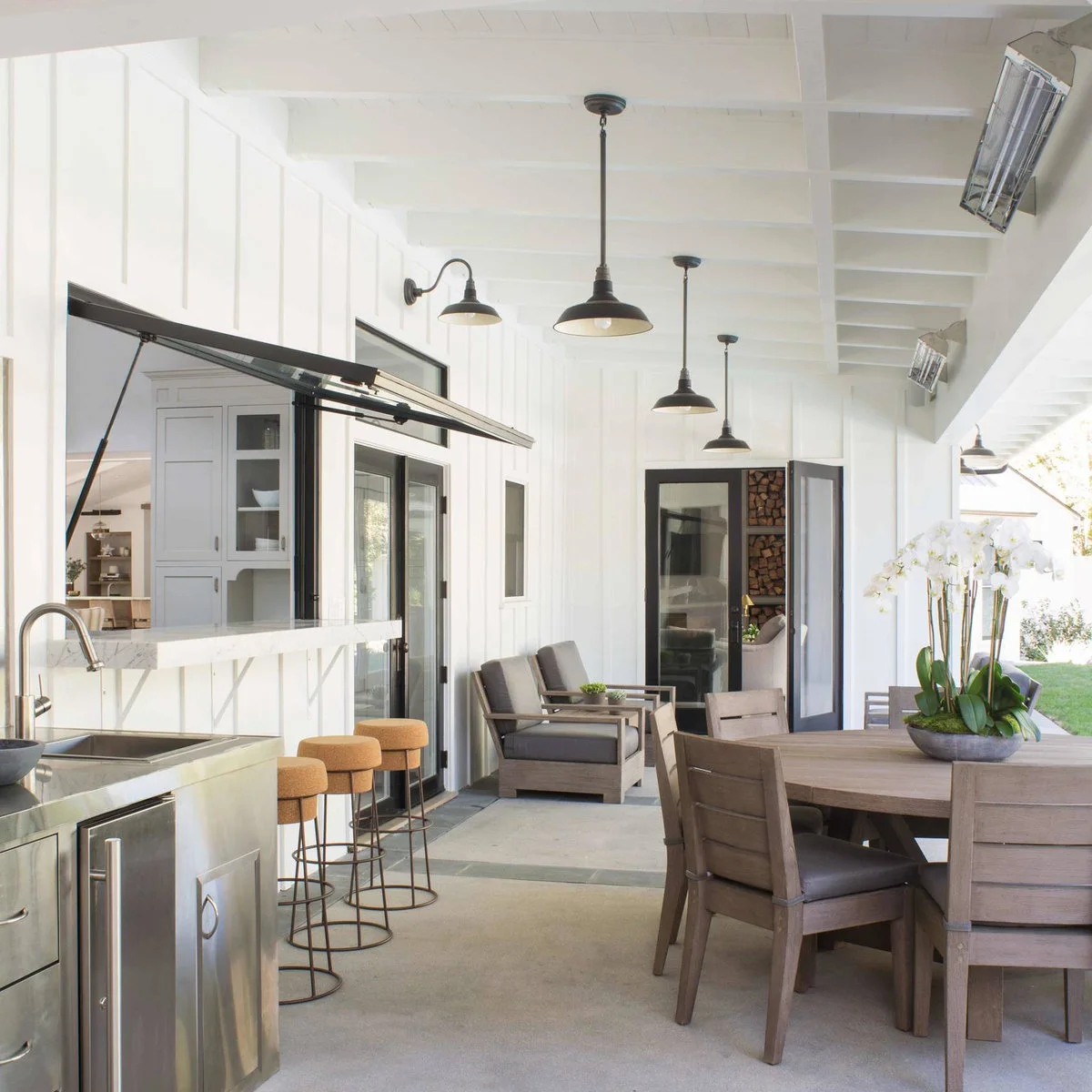 White covered patio with a lift-up serving window, three backless stools, a sink and a separate dining table