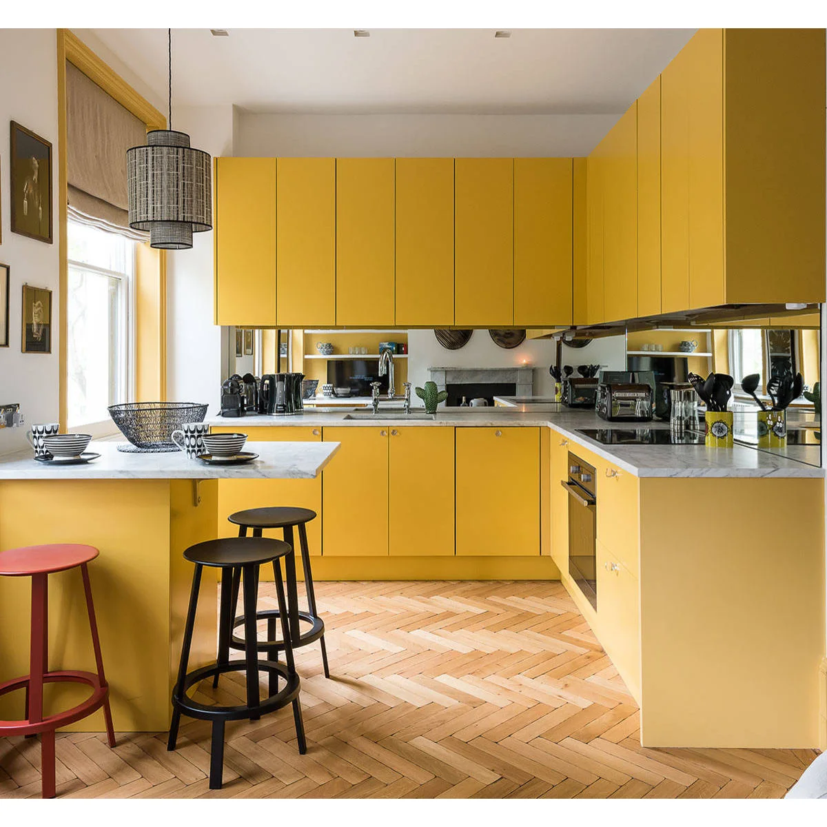 Mustard yellow kitchen cabinets with a mirrored backsplash, pale counters and black stools