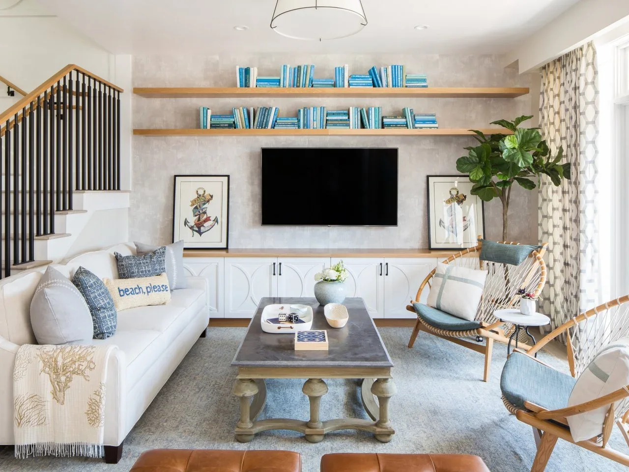 White fitted media cupboards with a timber top sit below a television and two long timber shelves filled with blue books.