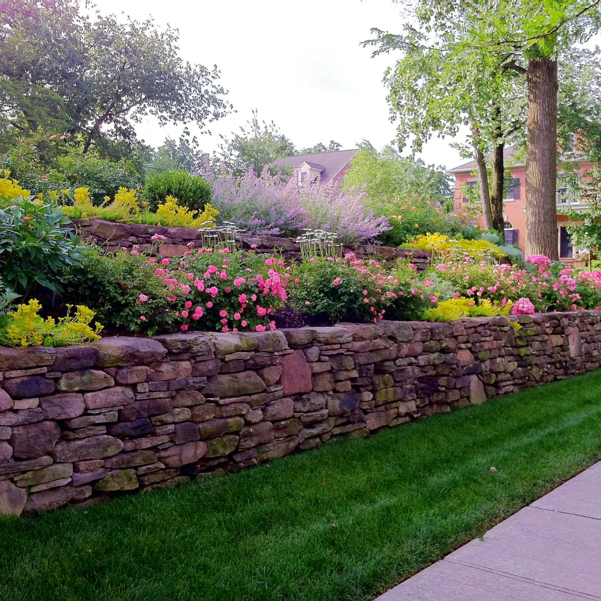 Two stone retaining levels with pink and purple flowers beside a garden path.