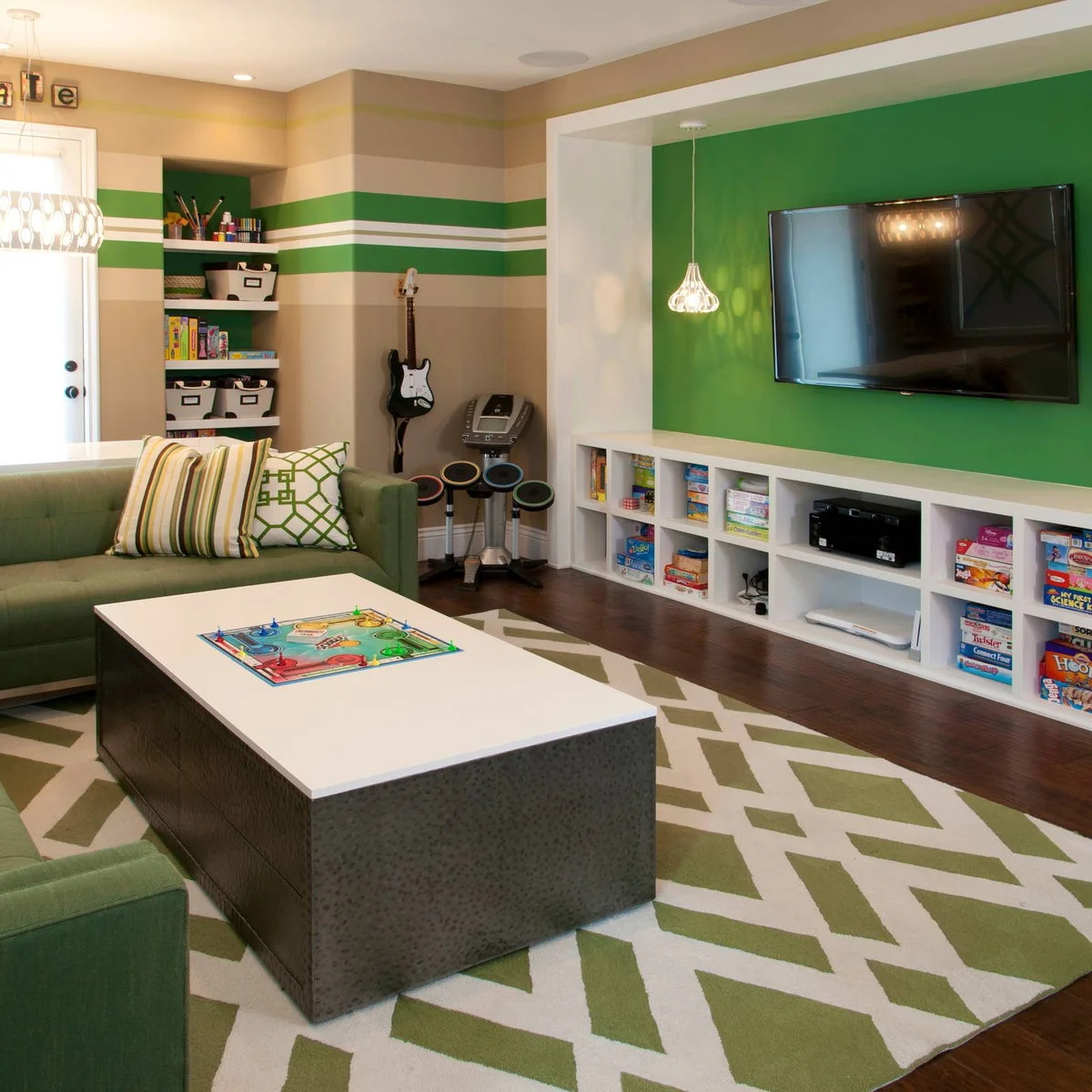 A green living room with a wall television, white cubby storage, a sectional sofa and board games on a low coffee table.