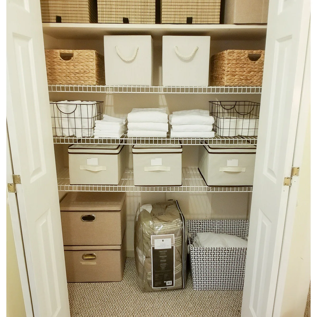 White wire linen shelves with stacked towels, woven baskets, lidded fabric boxes and spare bedding below