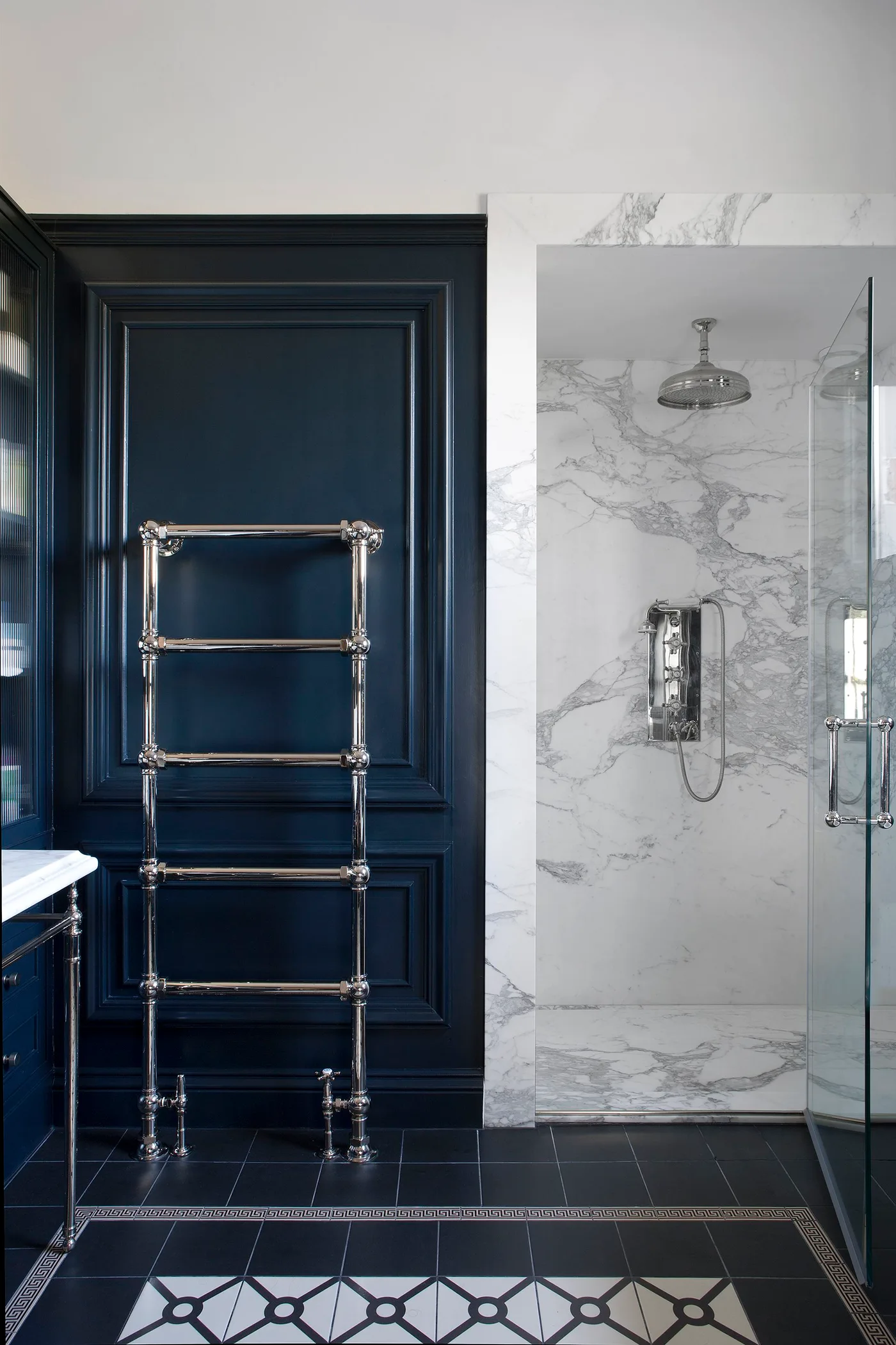 Deep blue paneled bathroom wall with a polished towel rail beside a pale veined shower enclosure.