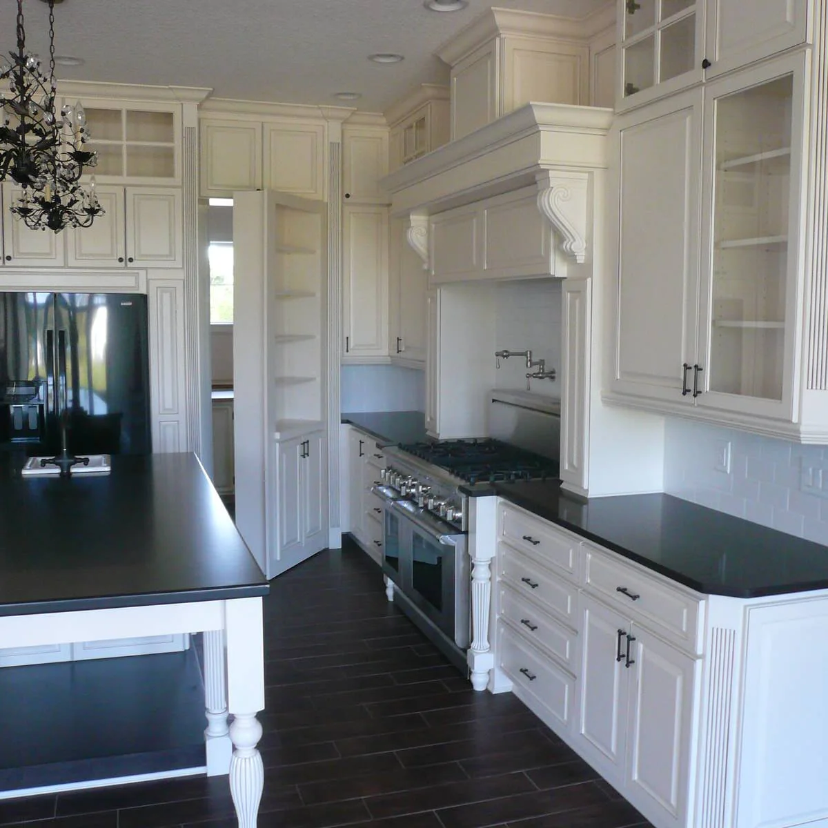A tall white paneled door stands open beside a refrigerator and cooking area, revealing shelving and a room beyond.