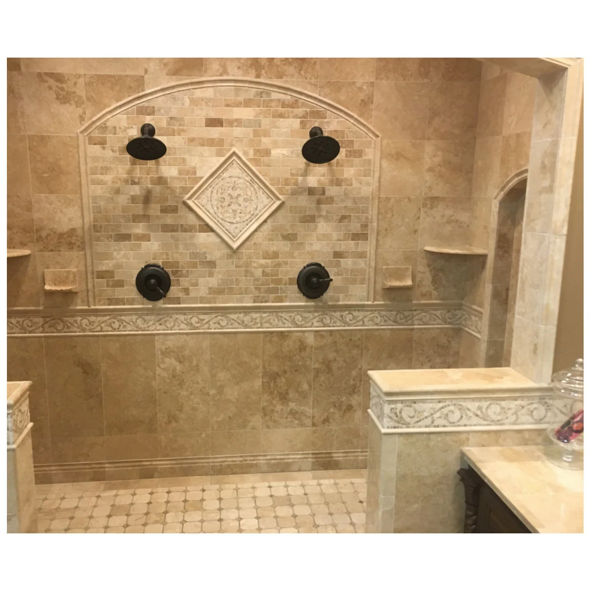 Warm tiled double shower with an arched mosaic panel, central diamond ornament and decorative border