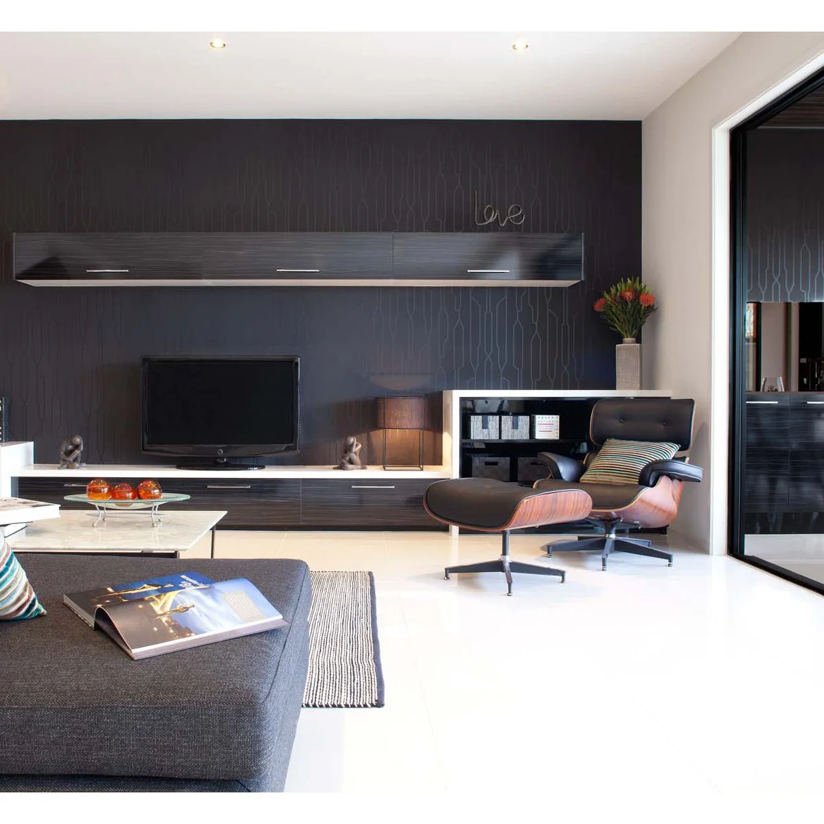 Dark patterned media wall with long low cabinets, a black lounge chair and pale floor