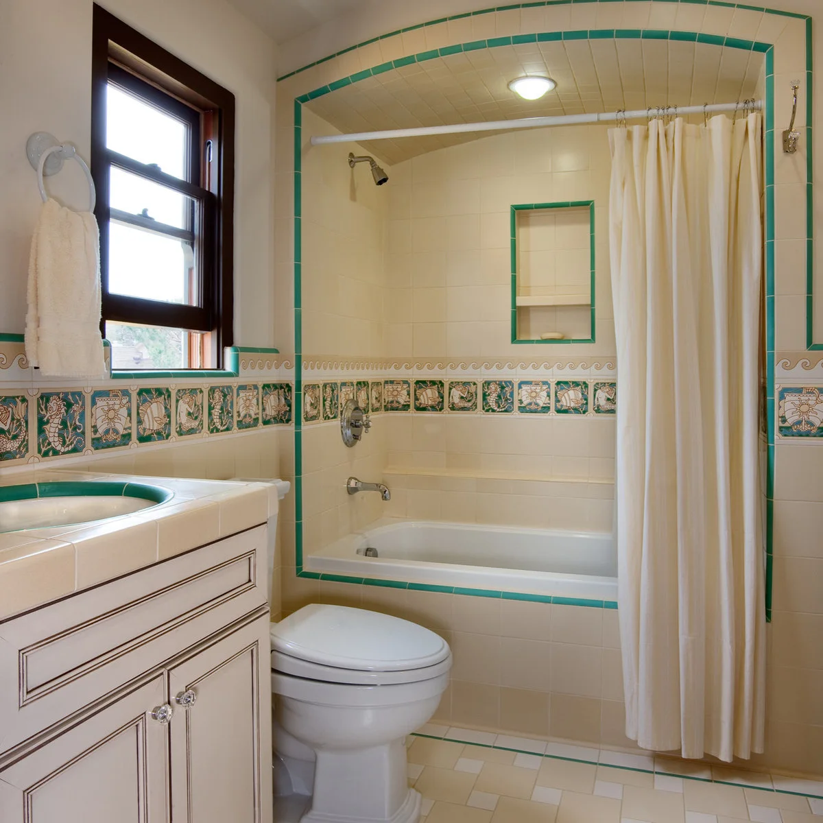 Cream tiled bathroom with green edging and an illustrated decorative band around the tub alcove