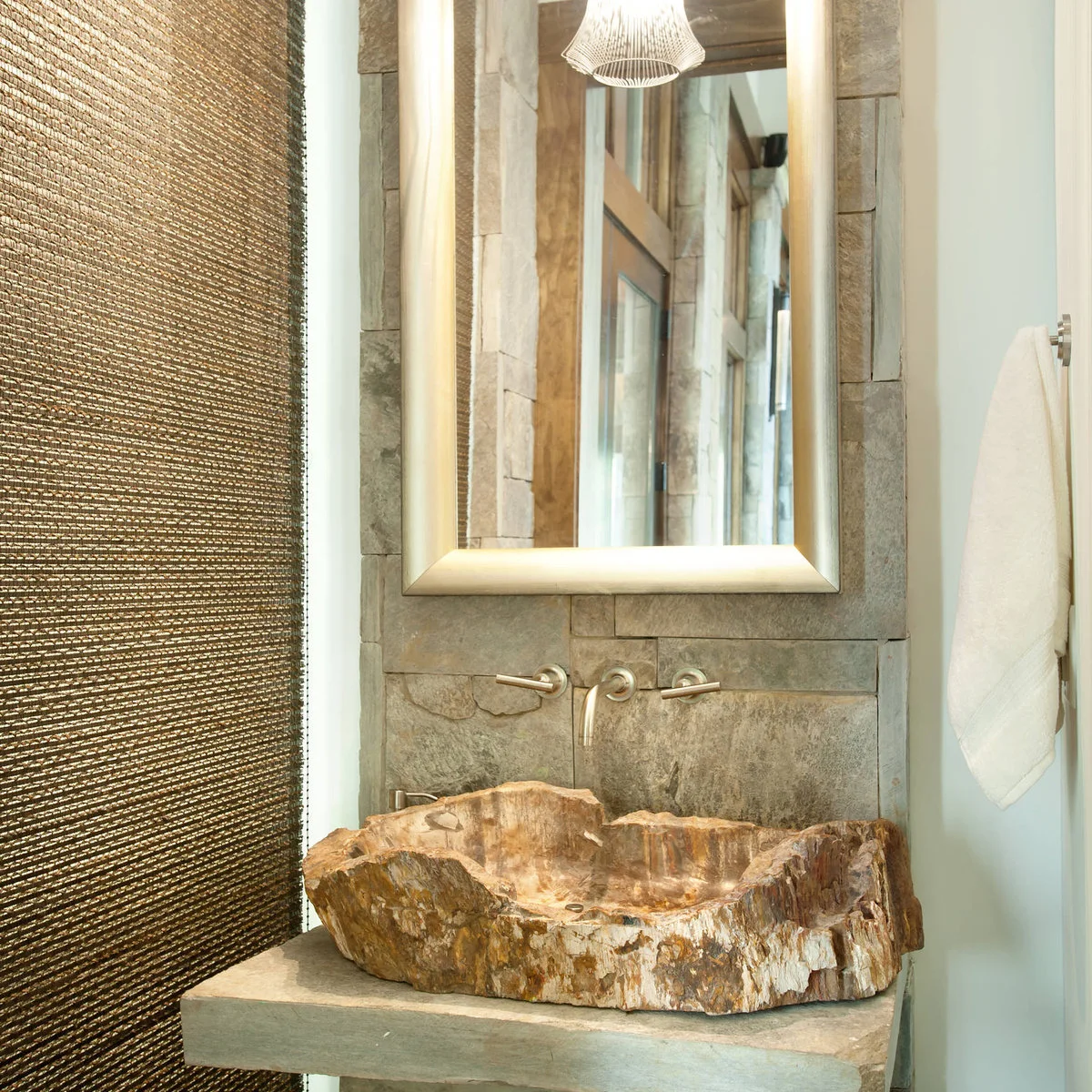 An irregular warm-toned vessel basin on a pale counter beneath a rectangular mirror and wall-mounted faucet.